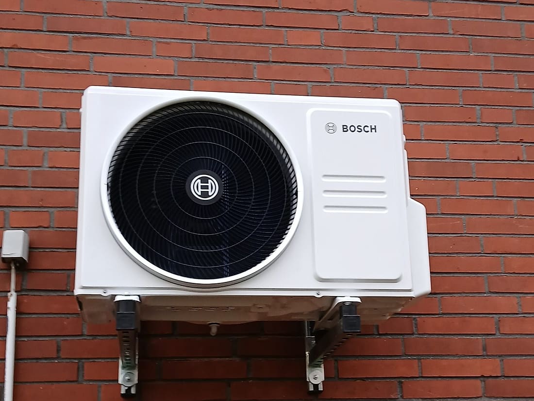 Außengerät einer Split-Klimaanlage, auf Wandkonsolen an einer roten Klinkerfassade montiert
