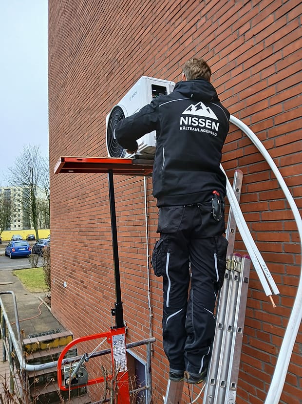 Kim Christian Nissen montiert ein Außengerät an einer Hausfassade