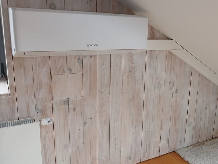 Innengerät einer Klimaanlage unter einer Dachschräge in einem holzverkleideten Raum